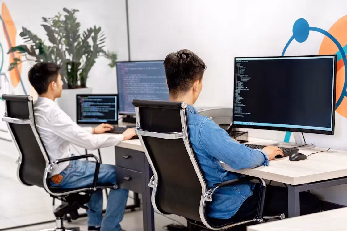 Developers working on their desktop PCs in office, with code displayed on their screens.